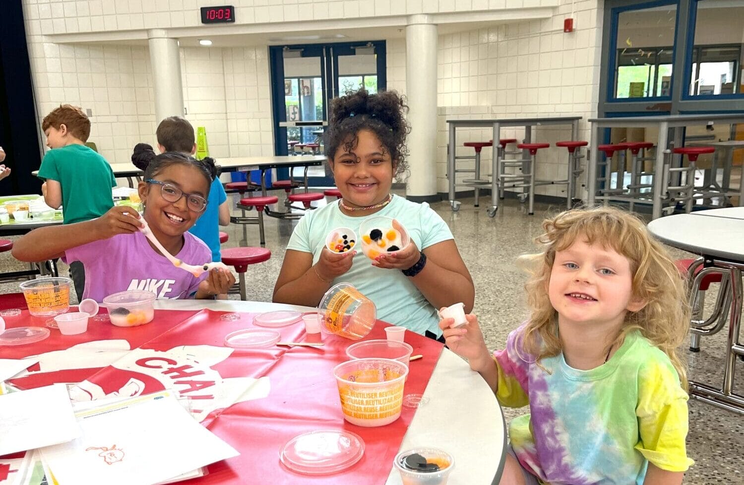 Group of three young girls making 'slime' together at a cafeteria table
