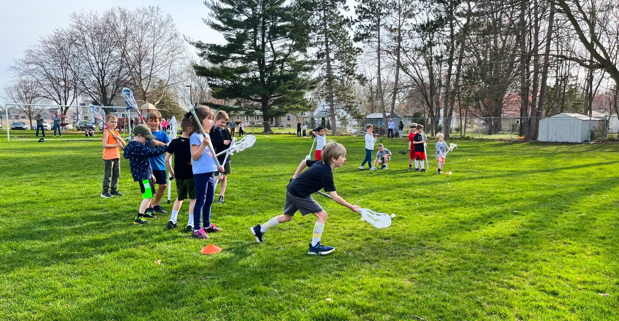 a group of kids outside with lacrosse sticks in their hands learning ball handling skills